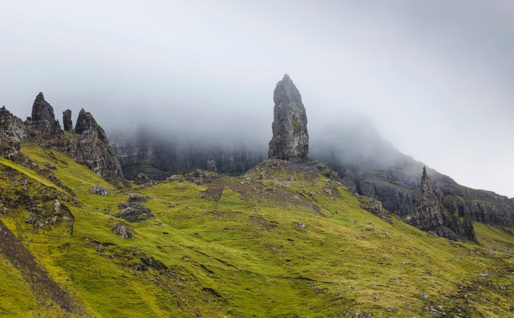 A jagged dark rock pinnacle stands on a hillside with dark misty cliffs behind it.