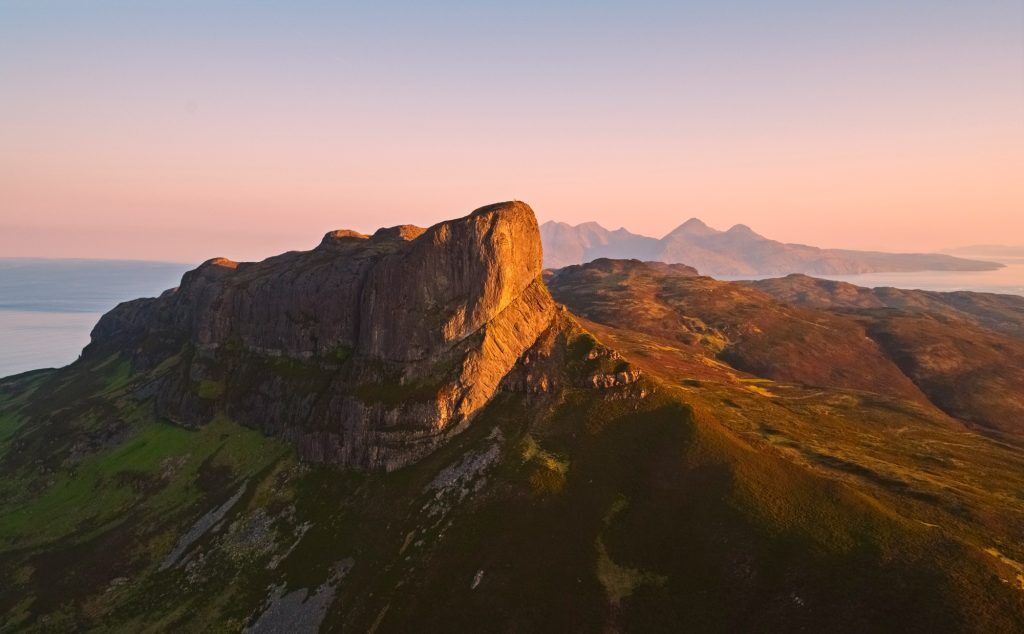 Soft sunlight hits a craggy rock peak. There is a mountainous island in the background.