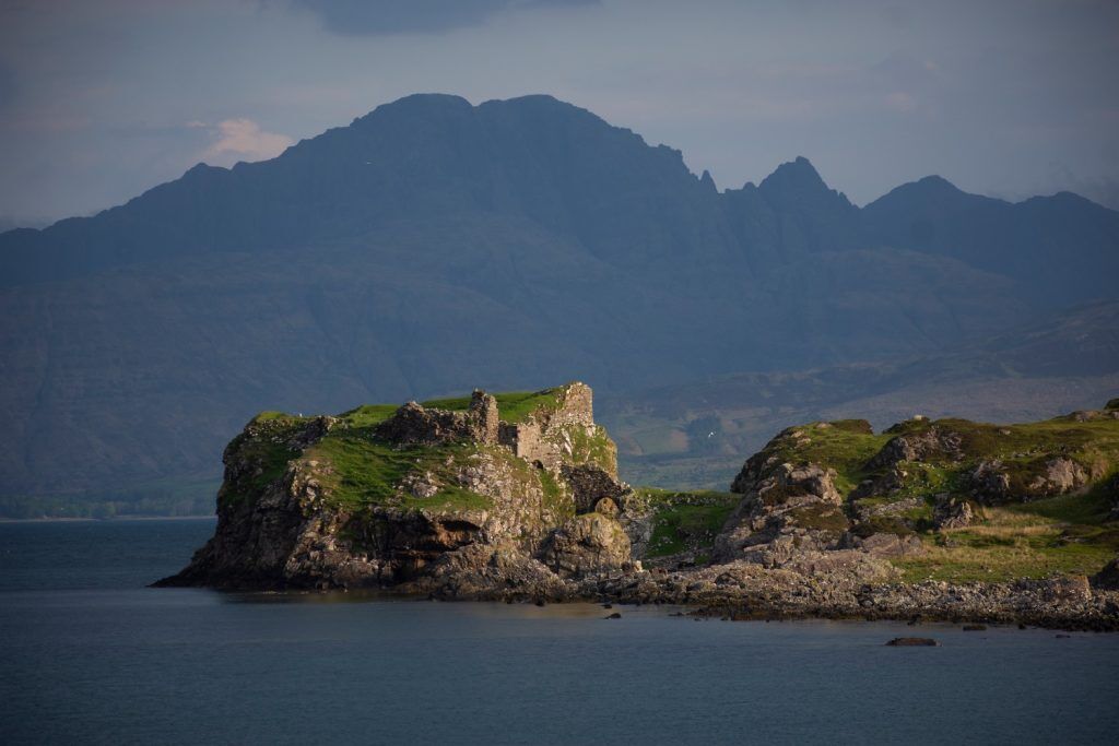 Castle ruins on a shoreline with mountains in the background